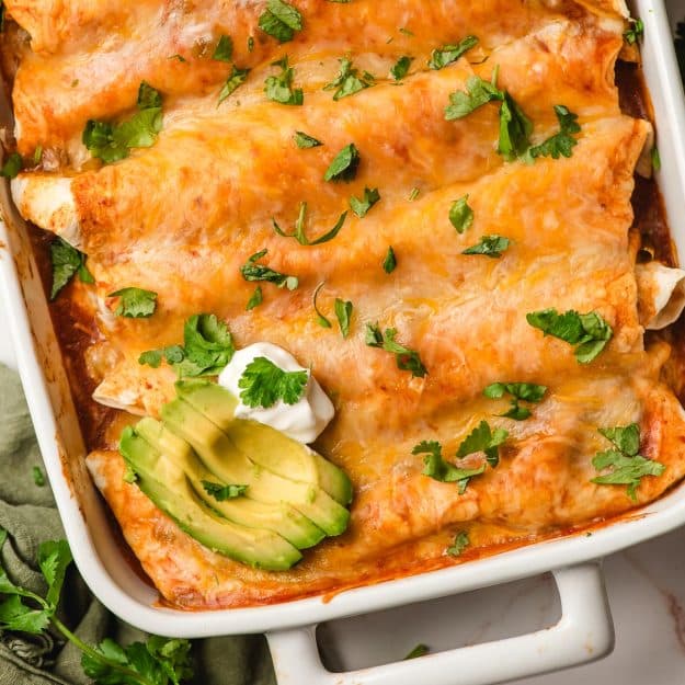 Cheesy chicken enchiladas with cilatnro and avocado in a casserole dish.