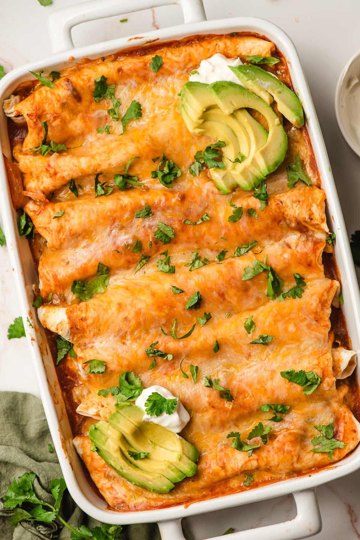 Cheesy chicken enchiladas with cilatnro and avocado in a casserole dish.