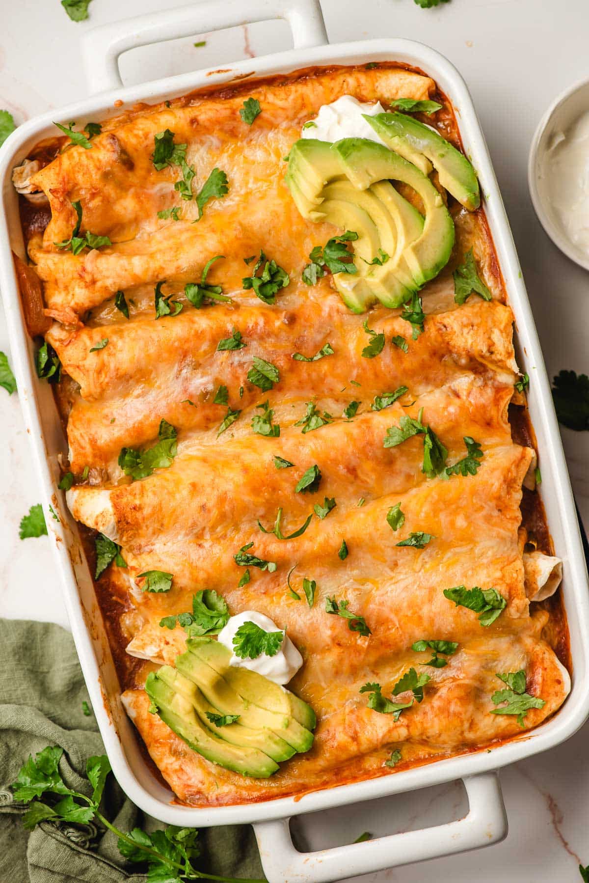 Crock Pot Chicken Enchiladas in a white casserole dish, topped with avocado slices.