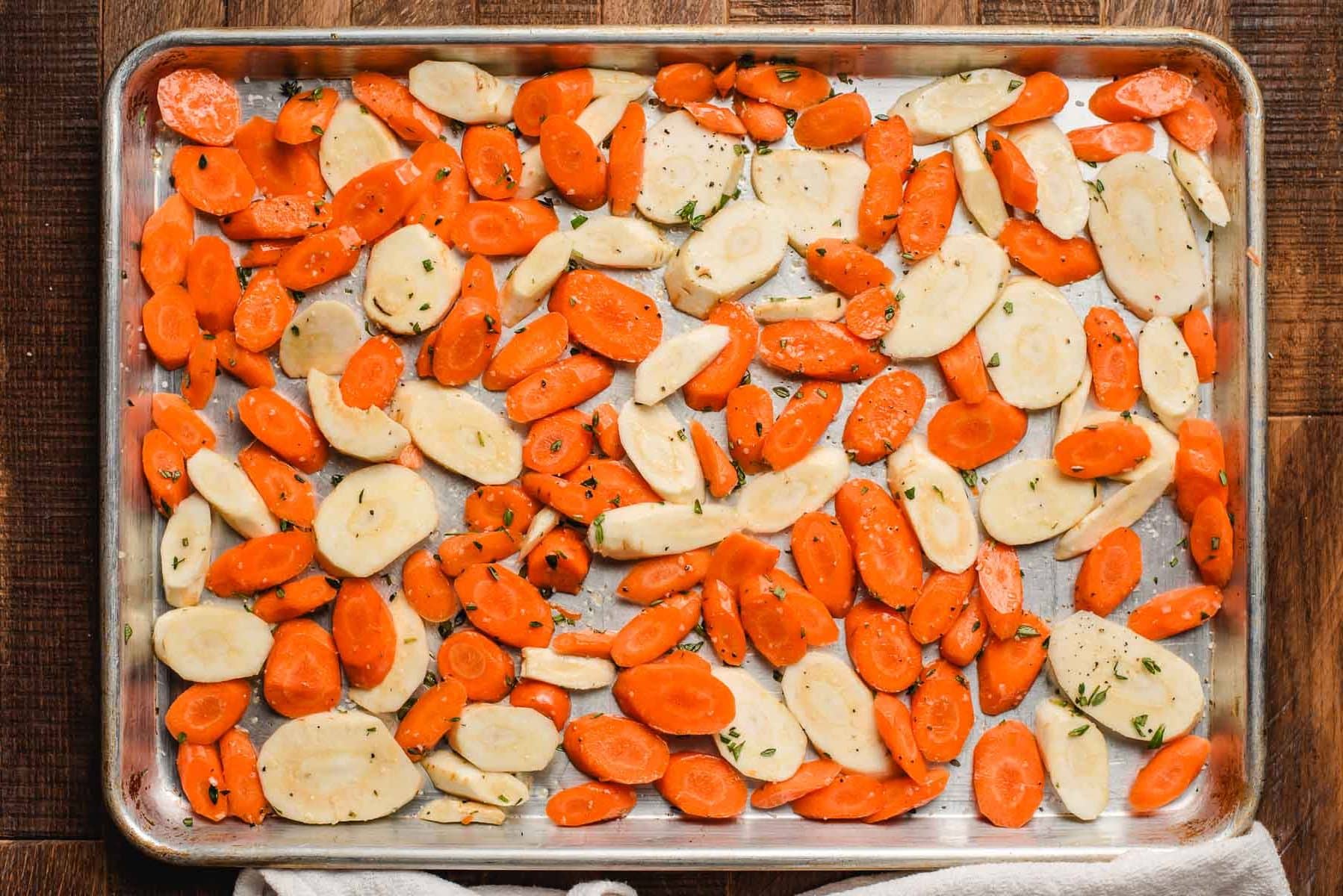 Sliced carrots and parsnips on a sheet pan ready to be roasted.