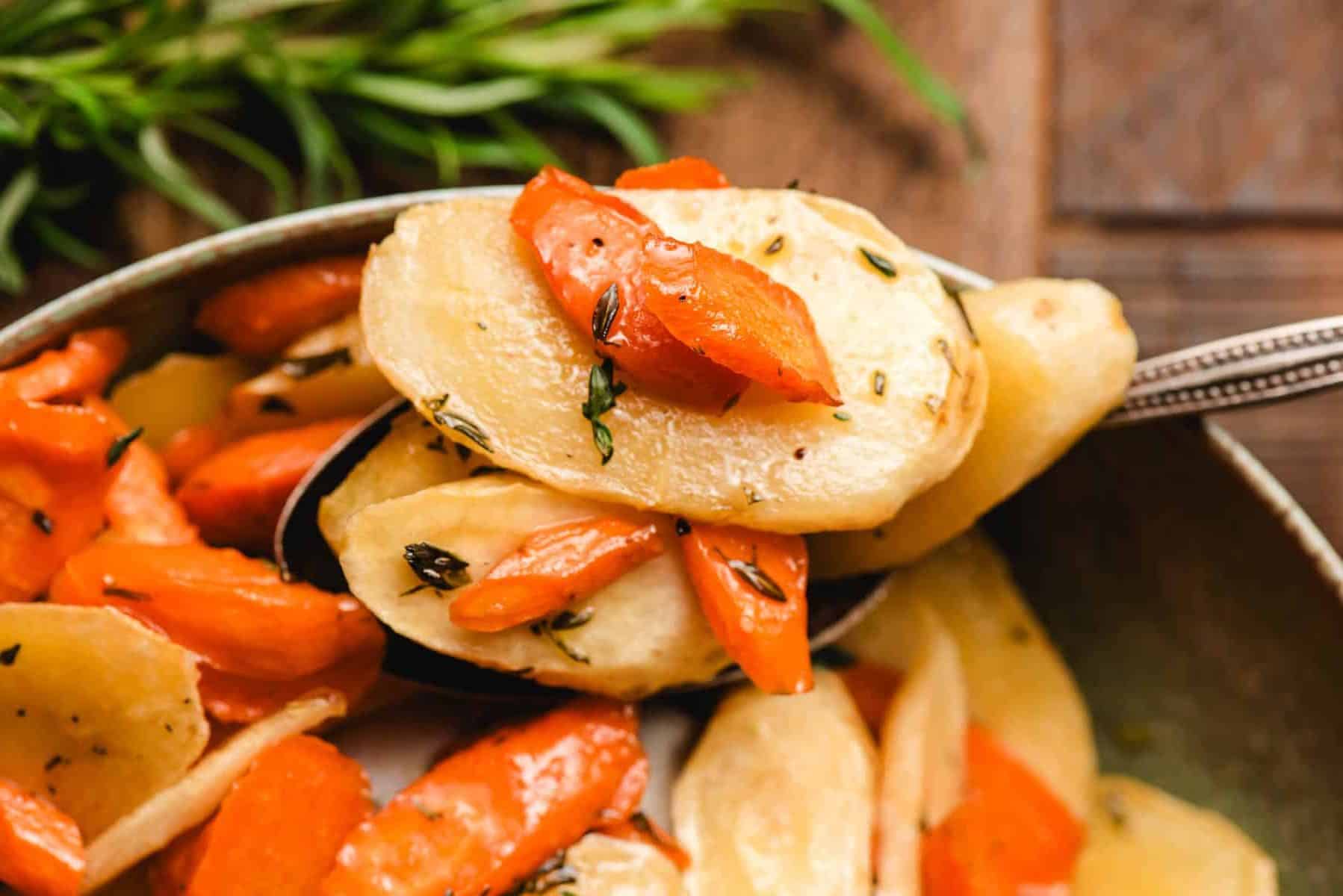 Spoon holding roasted parsnip and carrot slices topped with honey and thyme.