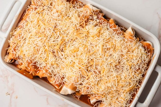 Chicken enchiladas topped with red sauce and shredded cheese in a casserole dish.