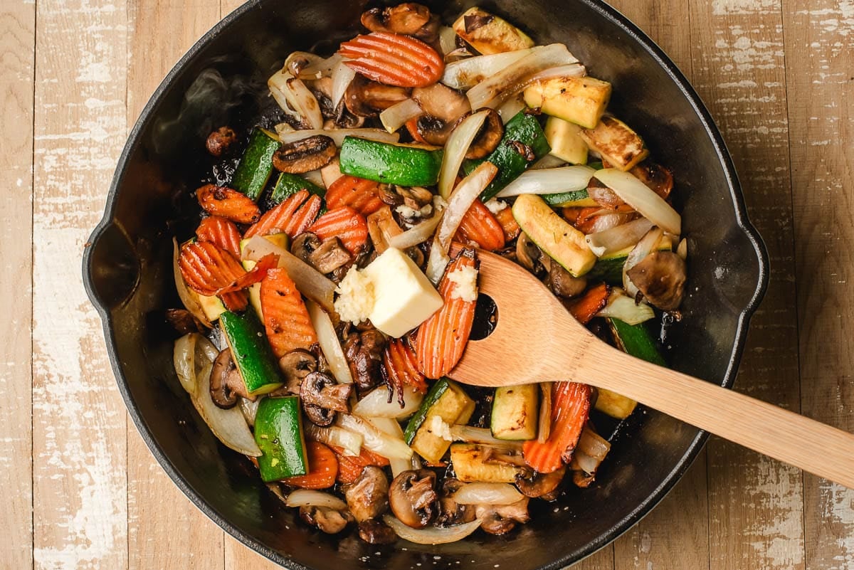 butter melting into the vegetables in the pan with a wooden spoon