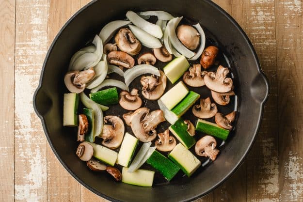 raw and cut veggies in a cast iron pan
