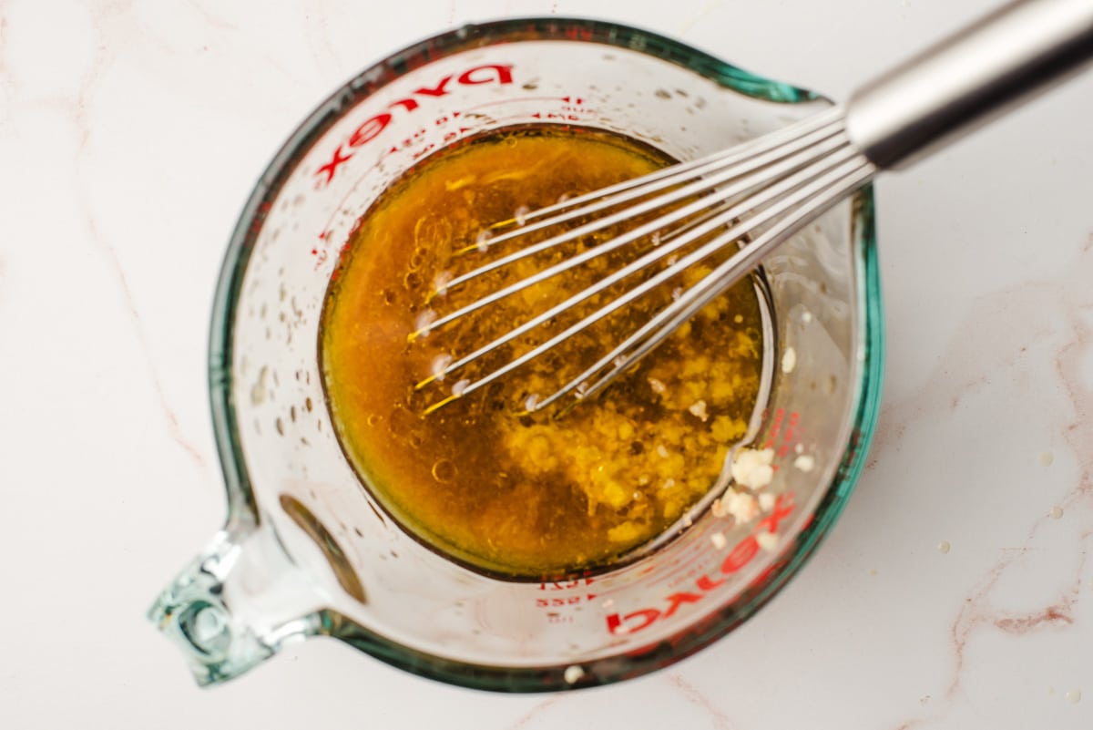 Orange juice, vinegar, olive oil, ginger, and salt in a glass measuring cup with a whisk.