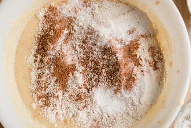 Flour, baking soda, baking powder, salt, and cinnamon sprinkled on batter in a mixing bowl.