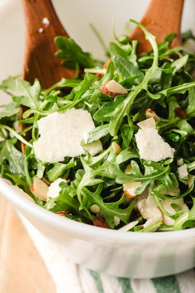 Wooden salad servers scooping up arugula salad.