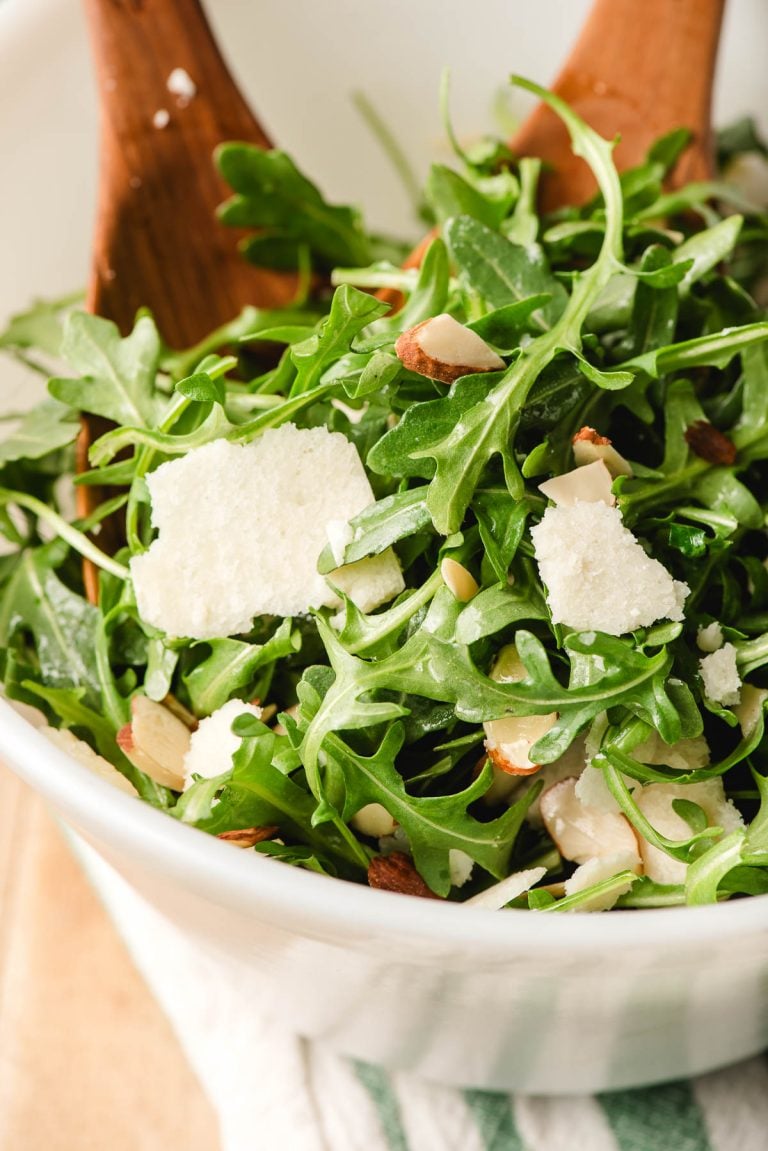 Wooden salad servers scooping up arugula salad.