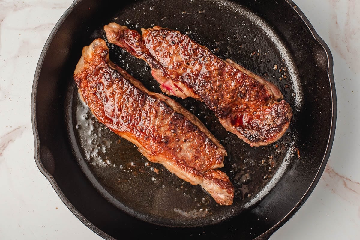 2 NY Strip Steaks المطبوخة في مقلاة حديدية.