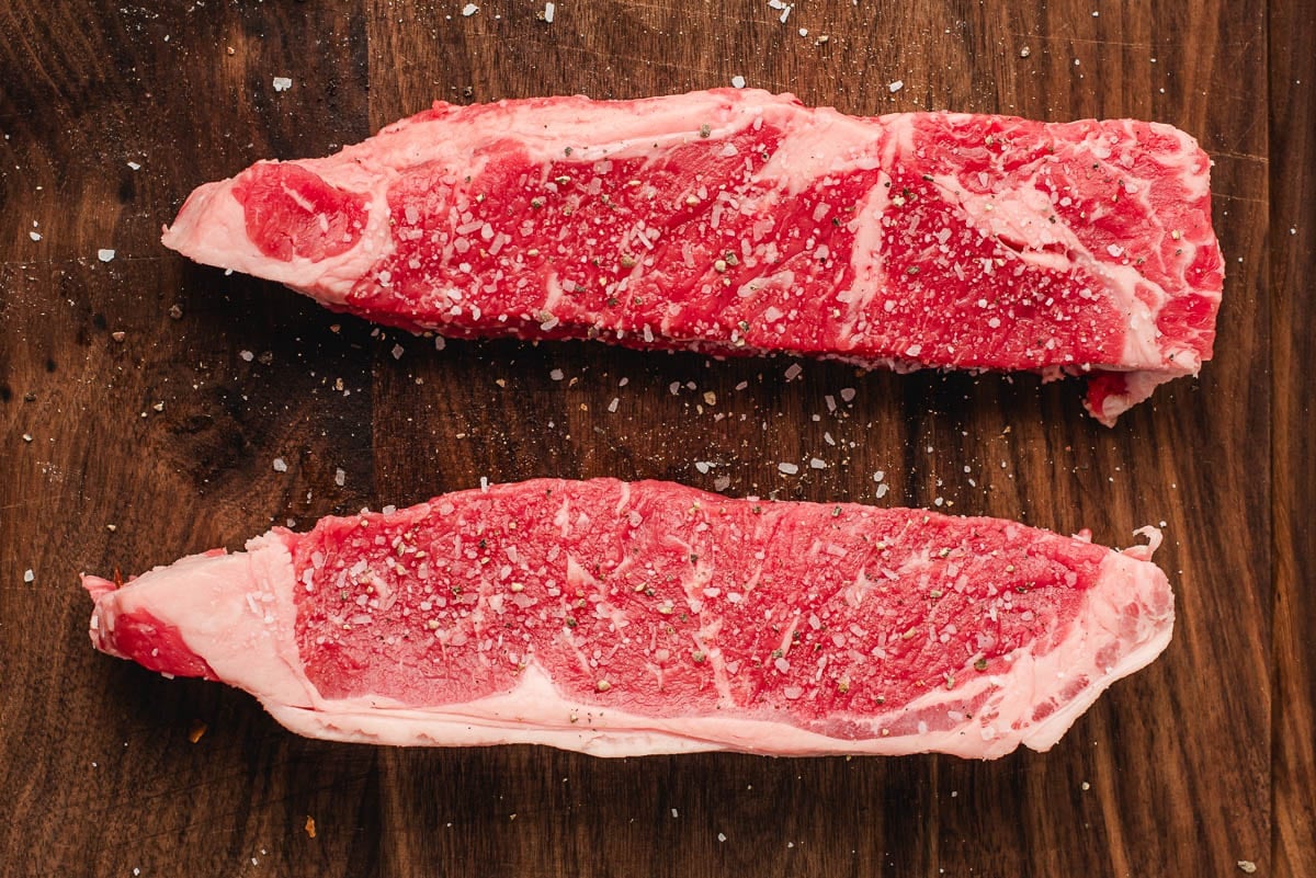 Raw NY Strip Steak على لوح التقطيع.