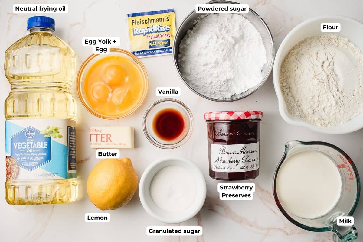 Vegetable oil, eggs, butter, lemon, sugar, powdered sugar, strawberry jam, milk, and flour on a white background.
