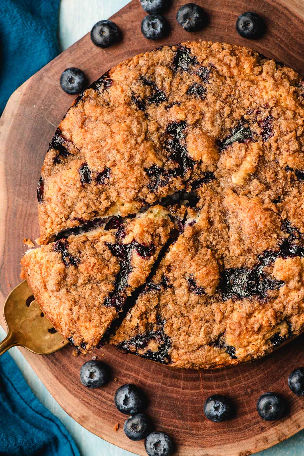 Blueberry sour cream coffee cake on a round wooden platter with one slice cut.