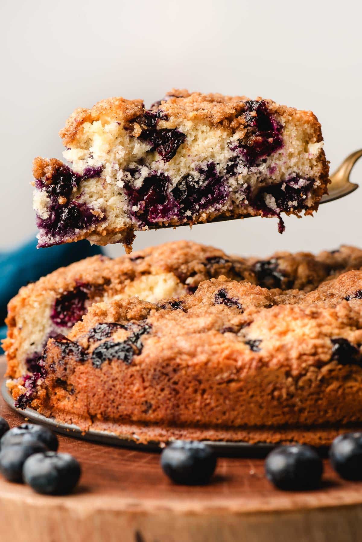 Gold pie server holding a slice of blueberry coffee cake.