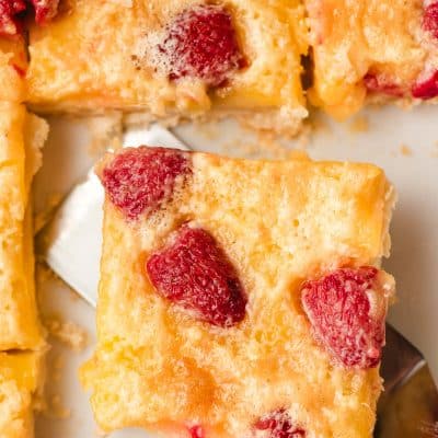 A close-up of a slice of a lemon raspberry bar being lifted by a spatula. Other slices are visible nearby.