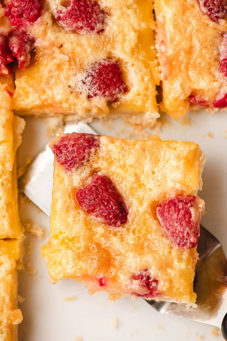A close-up of a slice of a lemon raspberry bar being lifted by a spatula. Other slices are visible nearby.