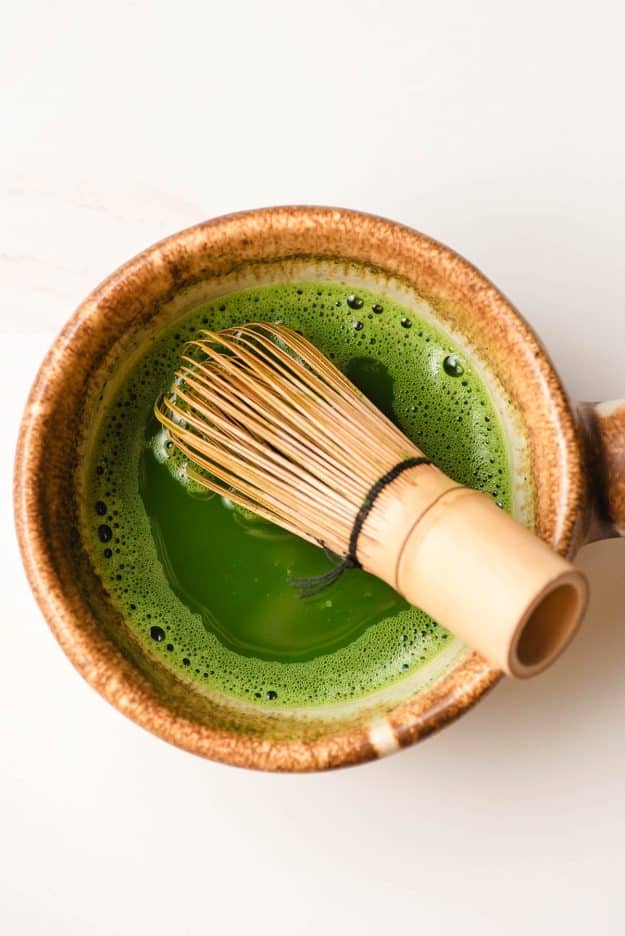 a small match bowl filled with water and matcha green tea powder with a bamboo whisk resting inside. 