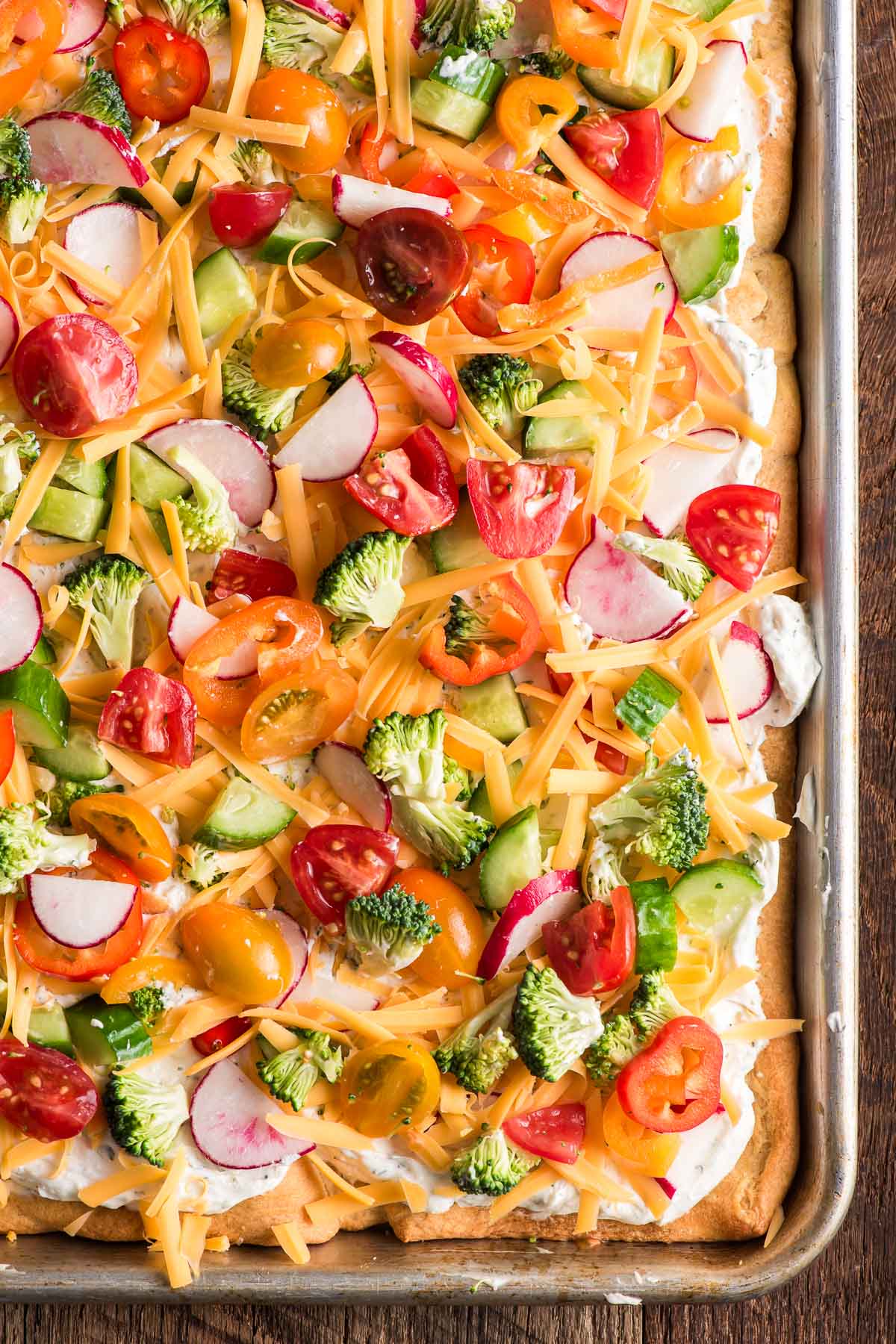 Overhead shot of cold veggie pizza with ranch cream cheese, cheddar, and fresh vegetables on a crescent roll crust