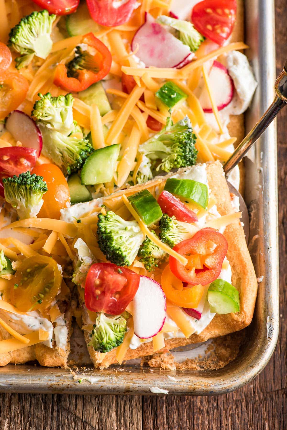 Fully assembled veggie pizza cut into squares for serving. 

