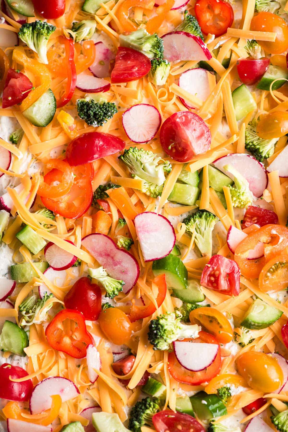 Sheet pan of sliced cold veggie pizza topped with colorful vegetables and creamy ranch spread.