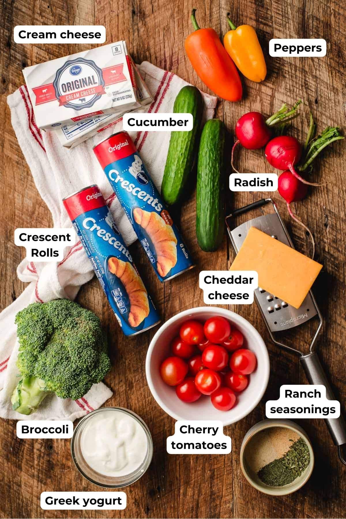 Ingredients laid out for making crescent roll vegetable pizza, including cream cheese, yogurt, seasonings, and chopped veggies.