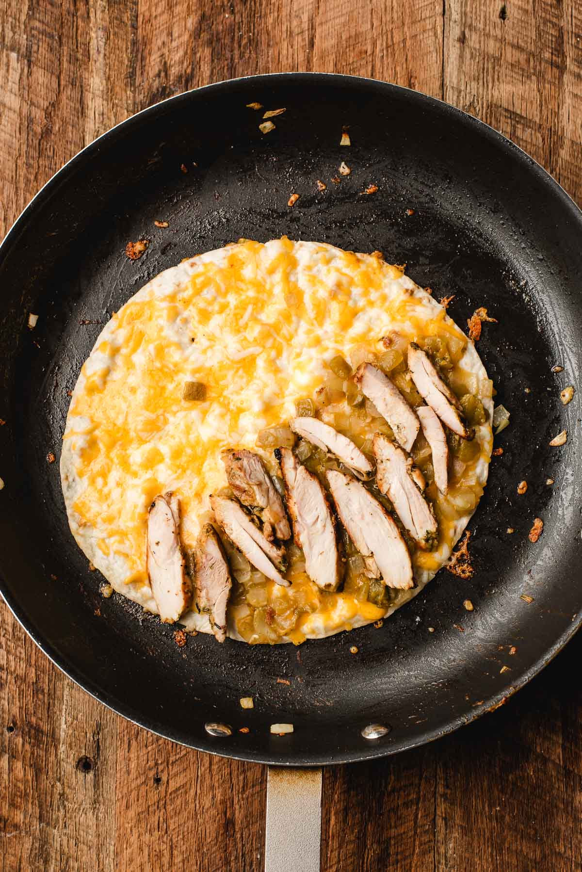 Open tortilla in skillet topped with cheese, chicken, and chile mixture before folding.