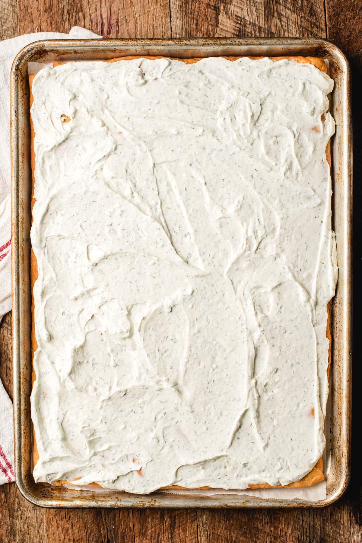 Creamy ranch spread being evenly smoothed over a cooled crescent roll crust.