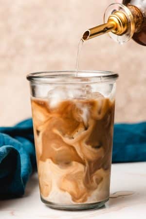 Cane sugar syrup being poured into iced coffee with cream.
