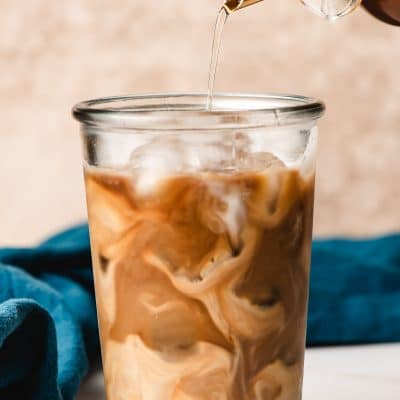 Cane sugar syrup being poured into iced coffee with cream.