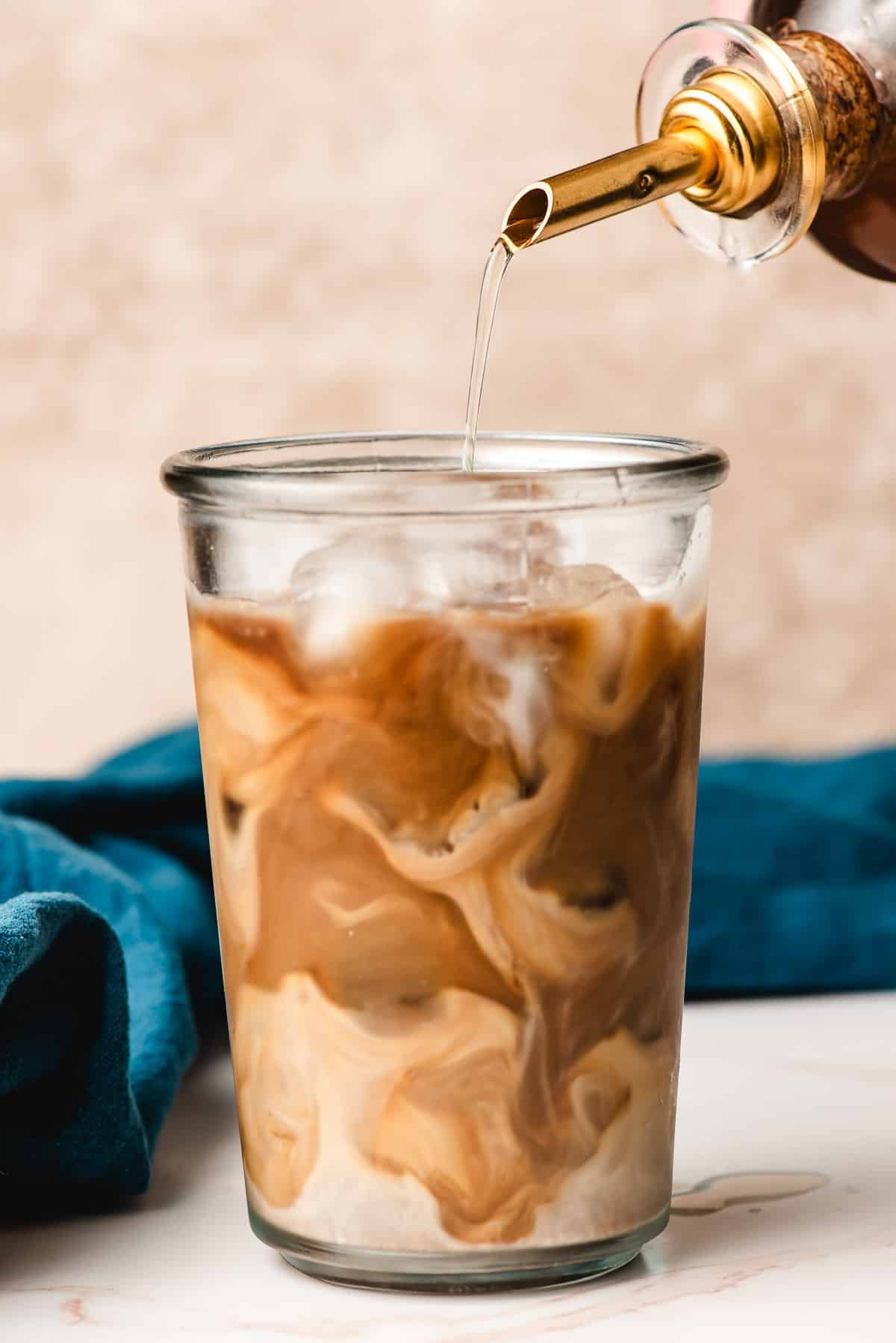 Cane sugar syrup being poured into iced coffee with cream.