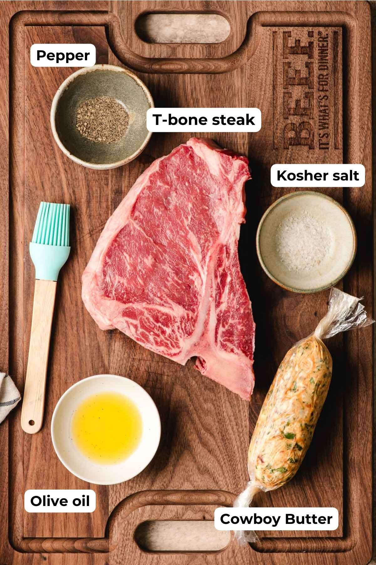 T-bone steak, bowl of olive oil, compound butter, and bowls of salt and pepper on a cutting board.