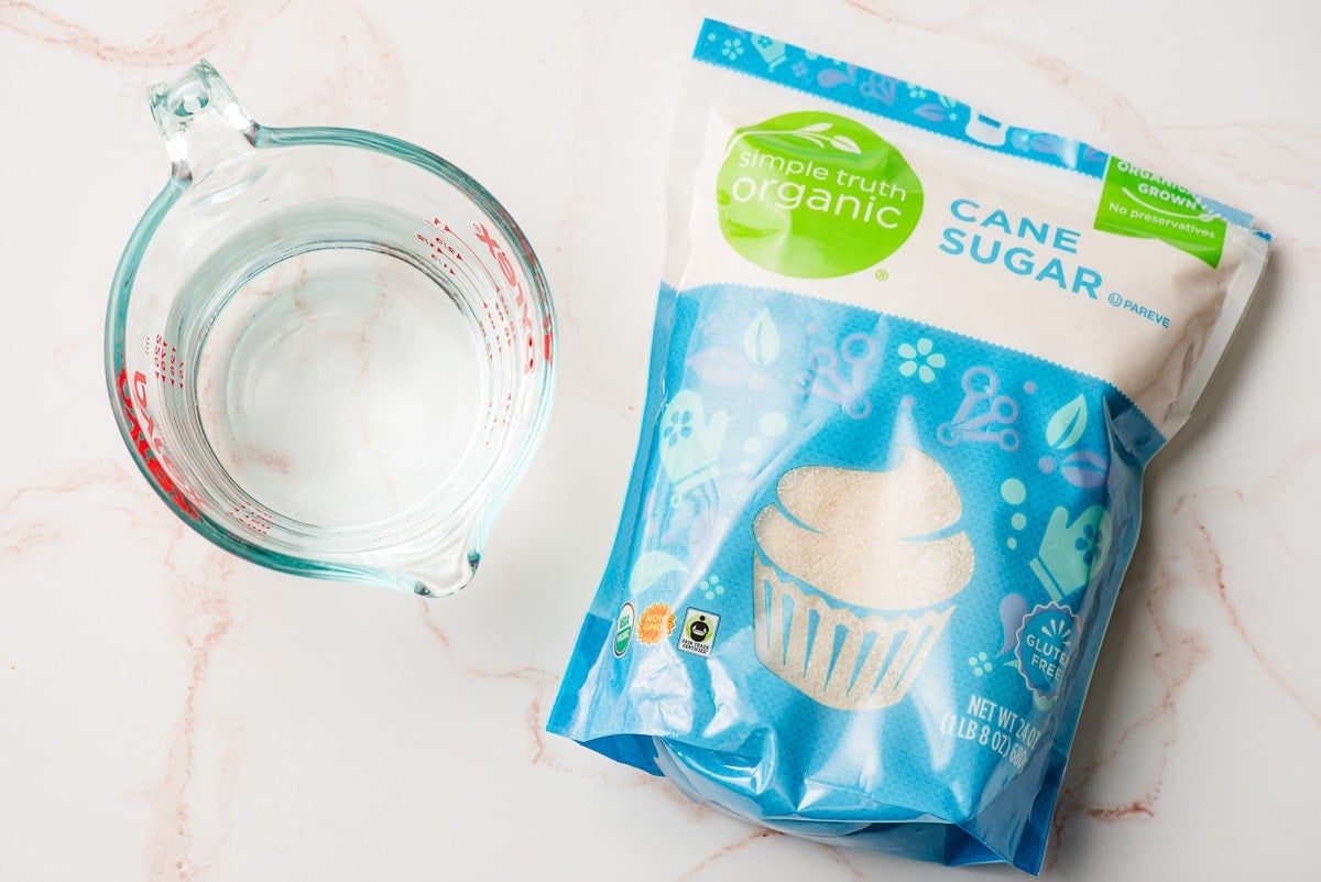 Measuring cup of water beside a bag of cane sugar.