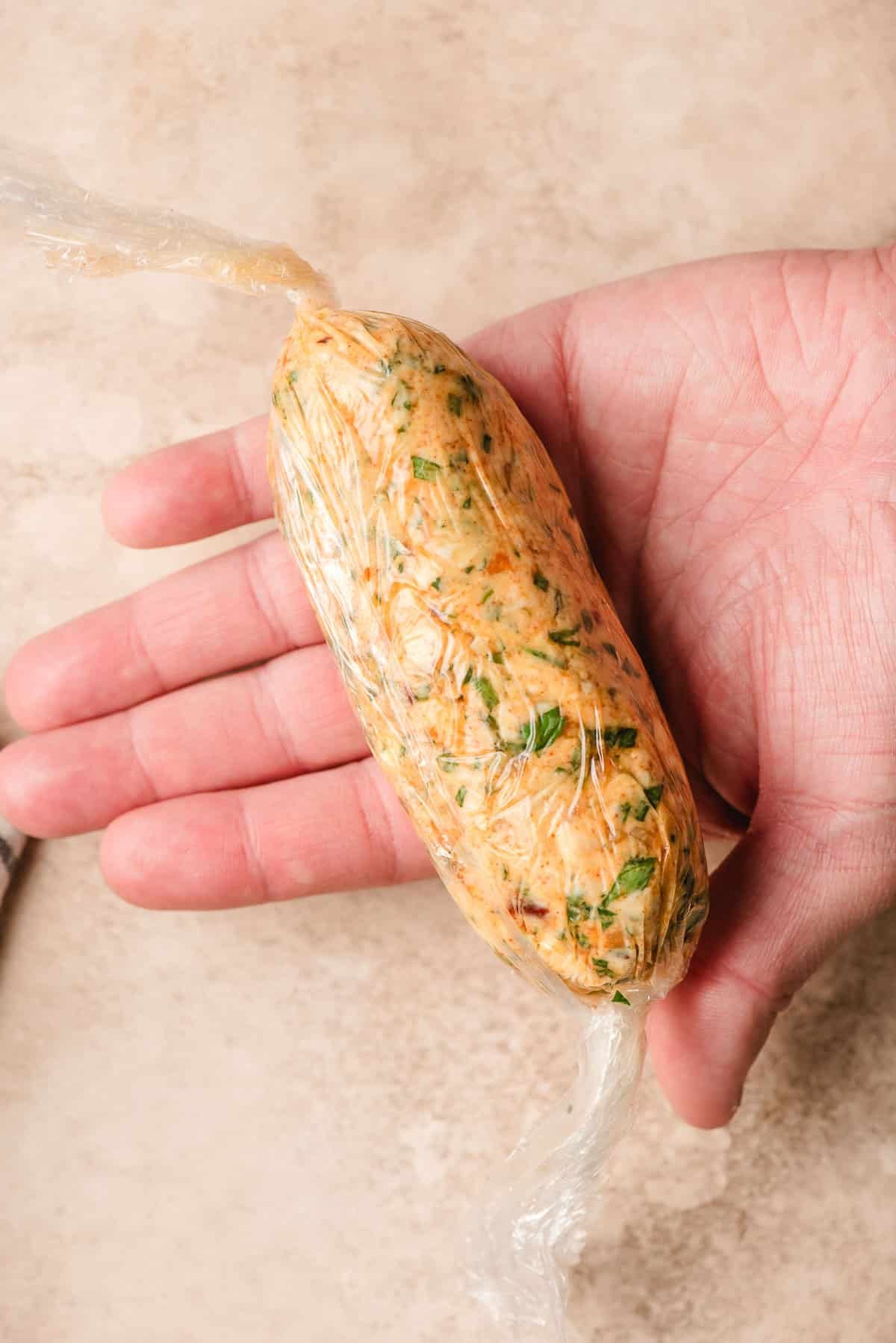 Hand holding a log of cowboy butter wrapped in saran wrap.