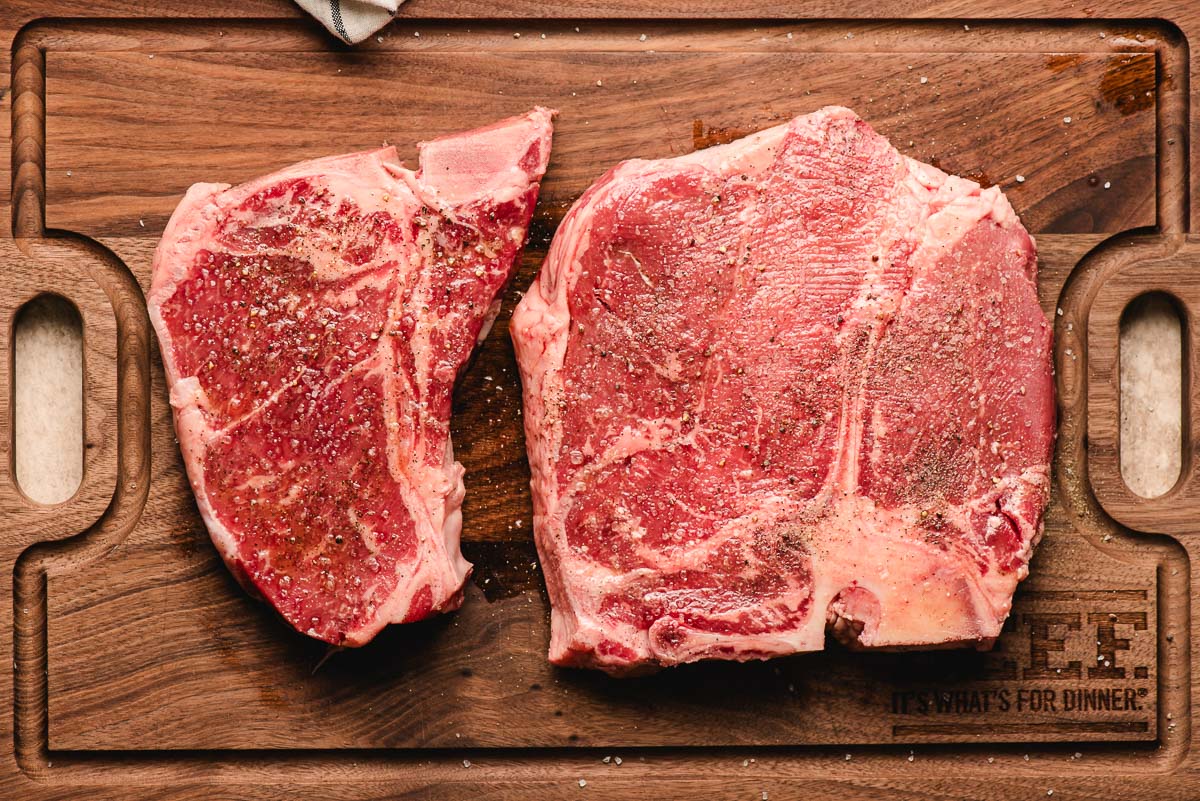T bone steak next to a porterhouse steak on a cutting board.
