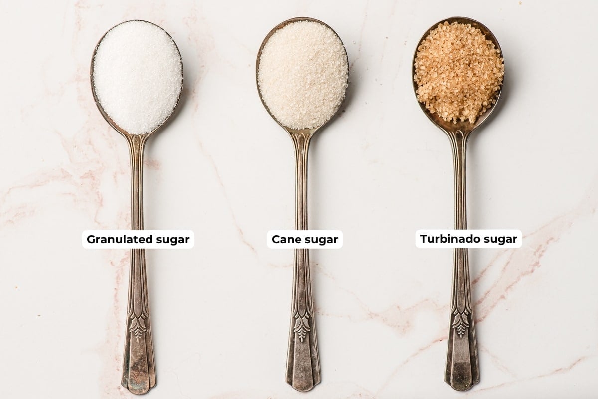 Three spoons, one with granulated sugar, one with cane sugar, and one with turbinado sugar.