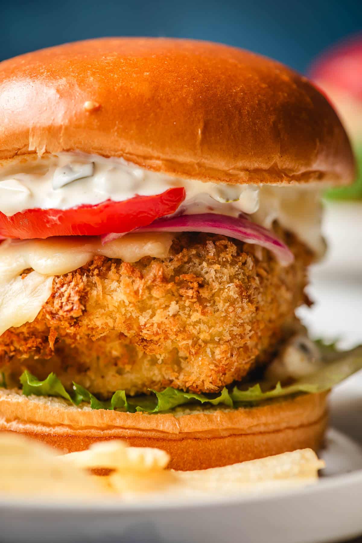 a close up of a cod fish sandwich with lettuce, tomato, onion, homemade tartar sauce, and an air fryer cod fillet 