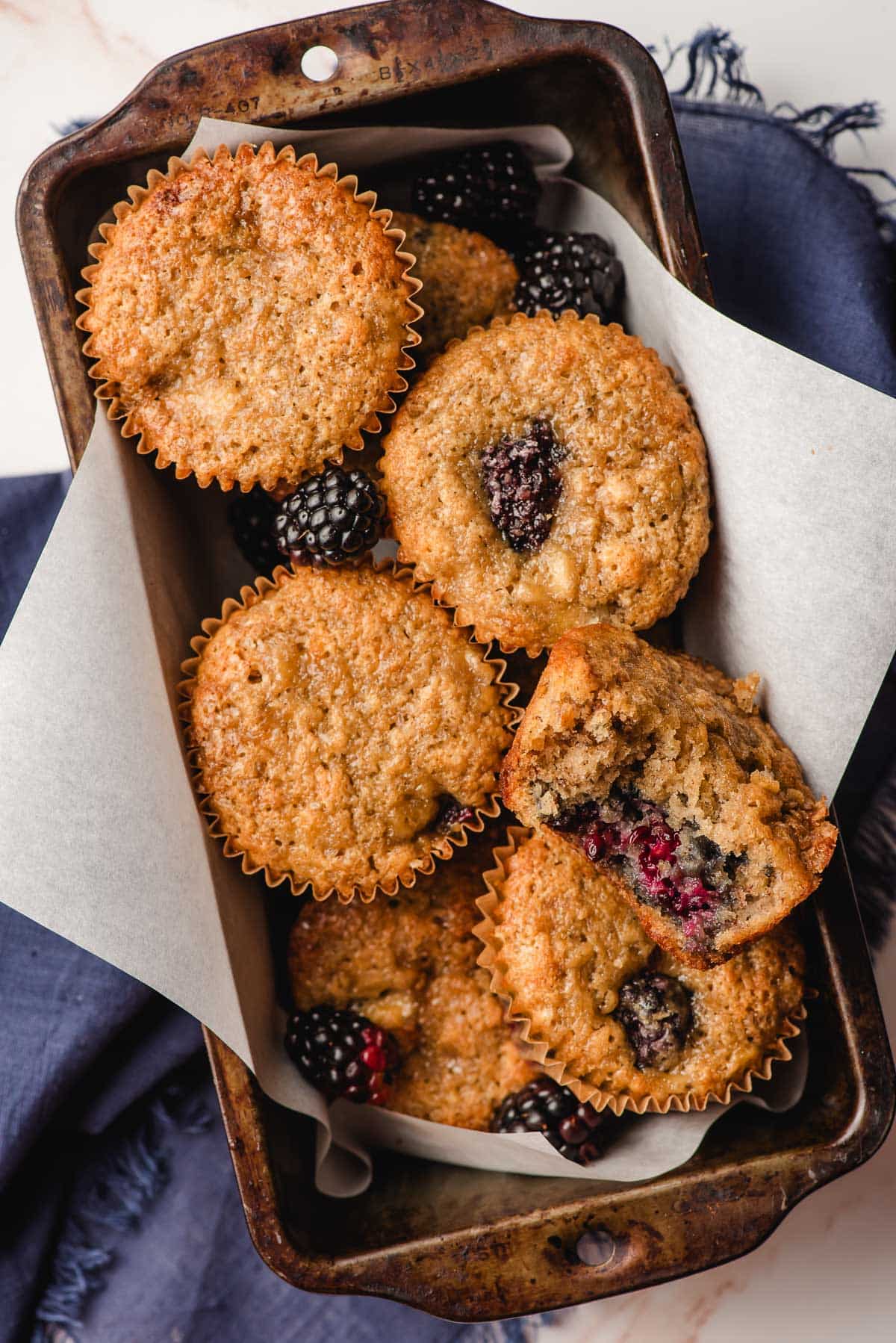 a loaf pan filled with fresh banana blackberry muffins with blackberries resting inside. One of the muffins has a bite taken out to show the middle.