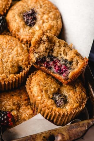 close up view of banana blackberry muffins with one muffin cut open to show the fluffy middle
