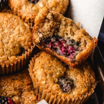close up view of banana blackberry muffins with one muffin cut open to show the fluffy middle