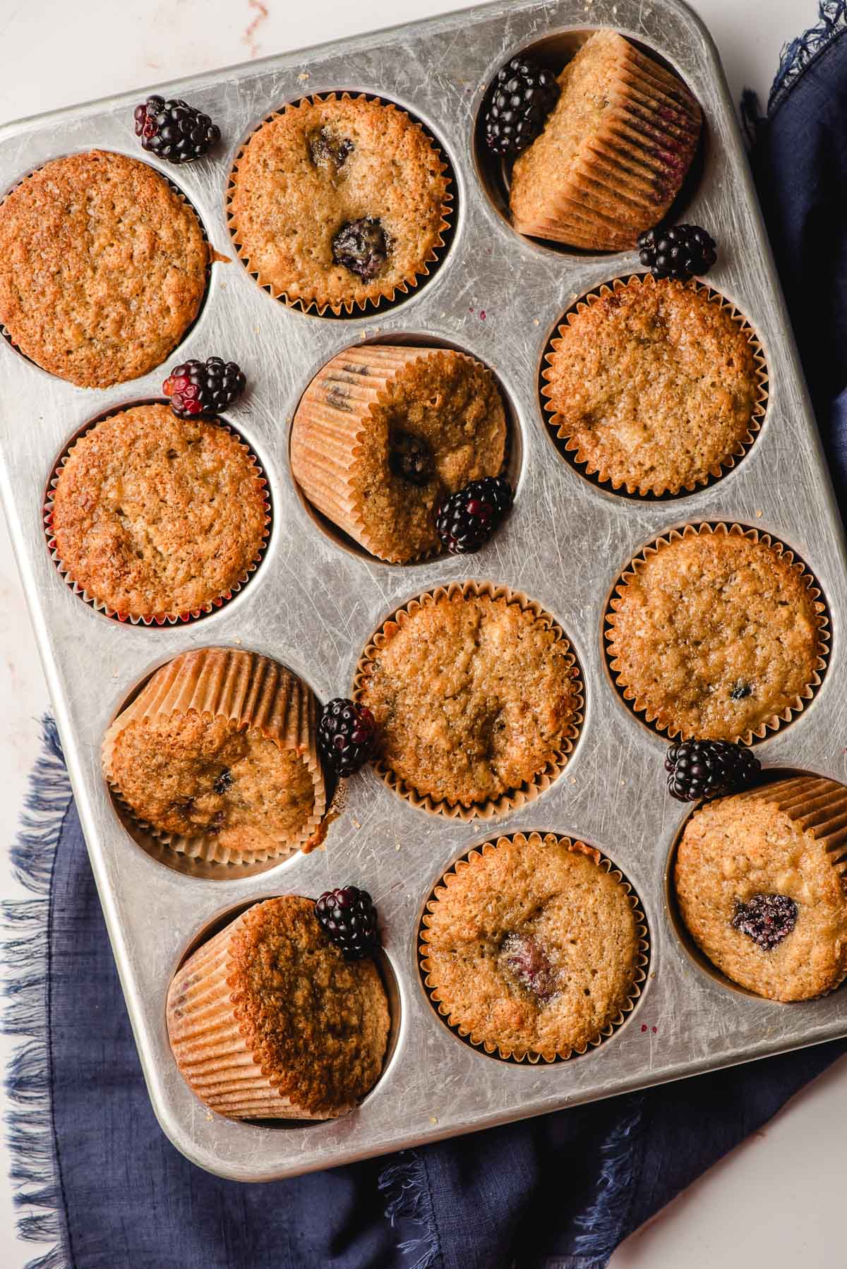 a styled shot of baked muffins in a tin decorated with fresh whole blackberries