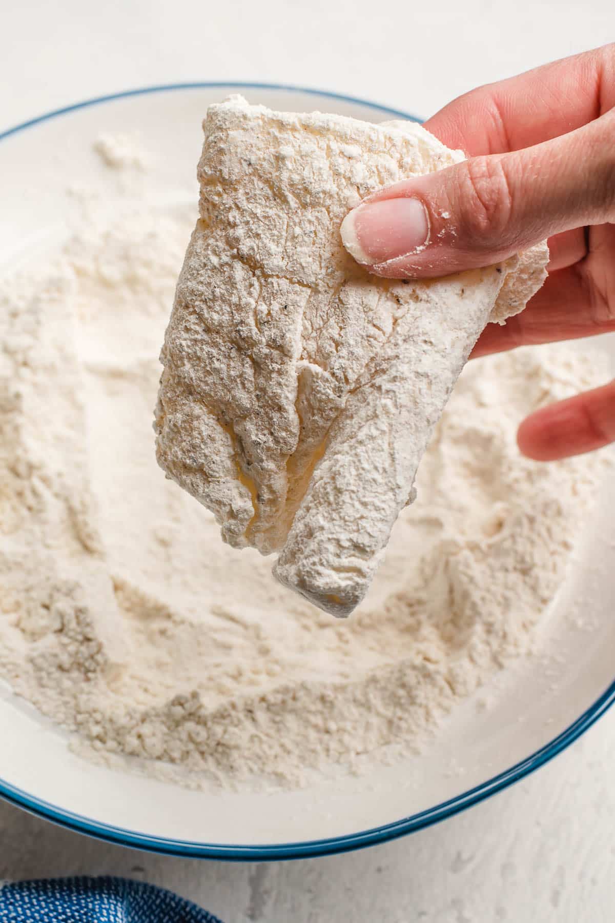 dipping a cod fillet into a bowl of flour