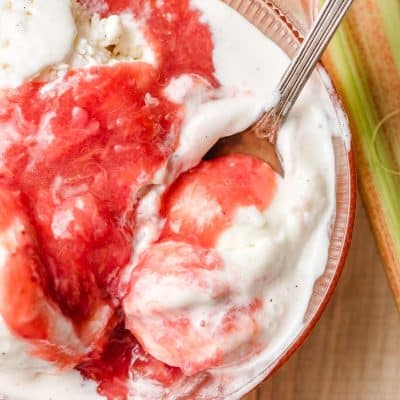 Spoon scooping up ice cream with strawberry rhubarb compote out of a bowl.