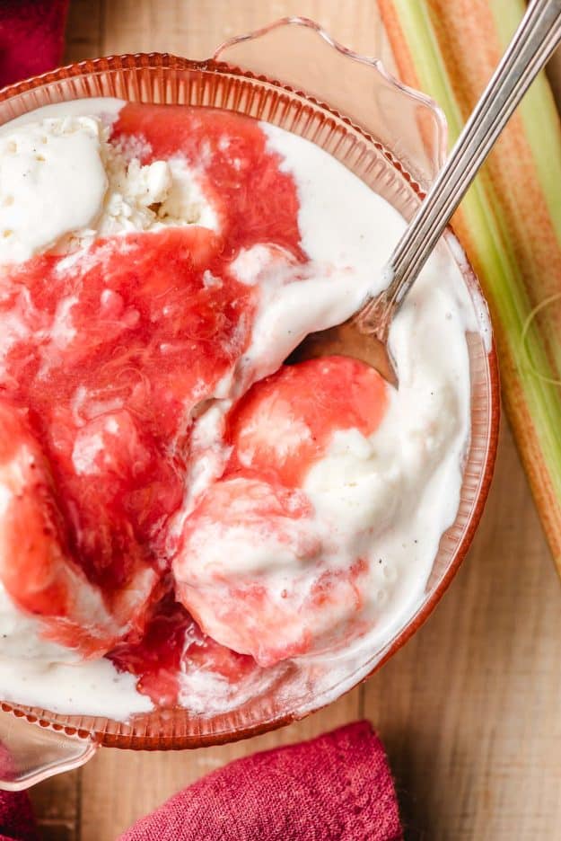Spoon scooping up ice cream with strawberry rhubarb compote out of a bowl.