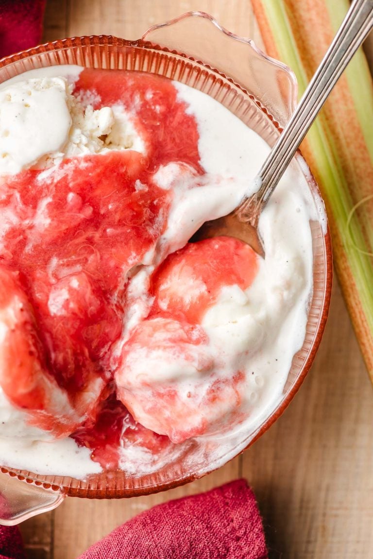 Spoon scooping up ice cream with strawberry rhubarb compote out of a bowl.