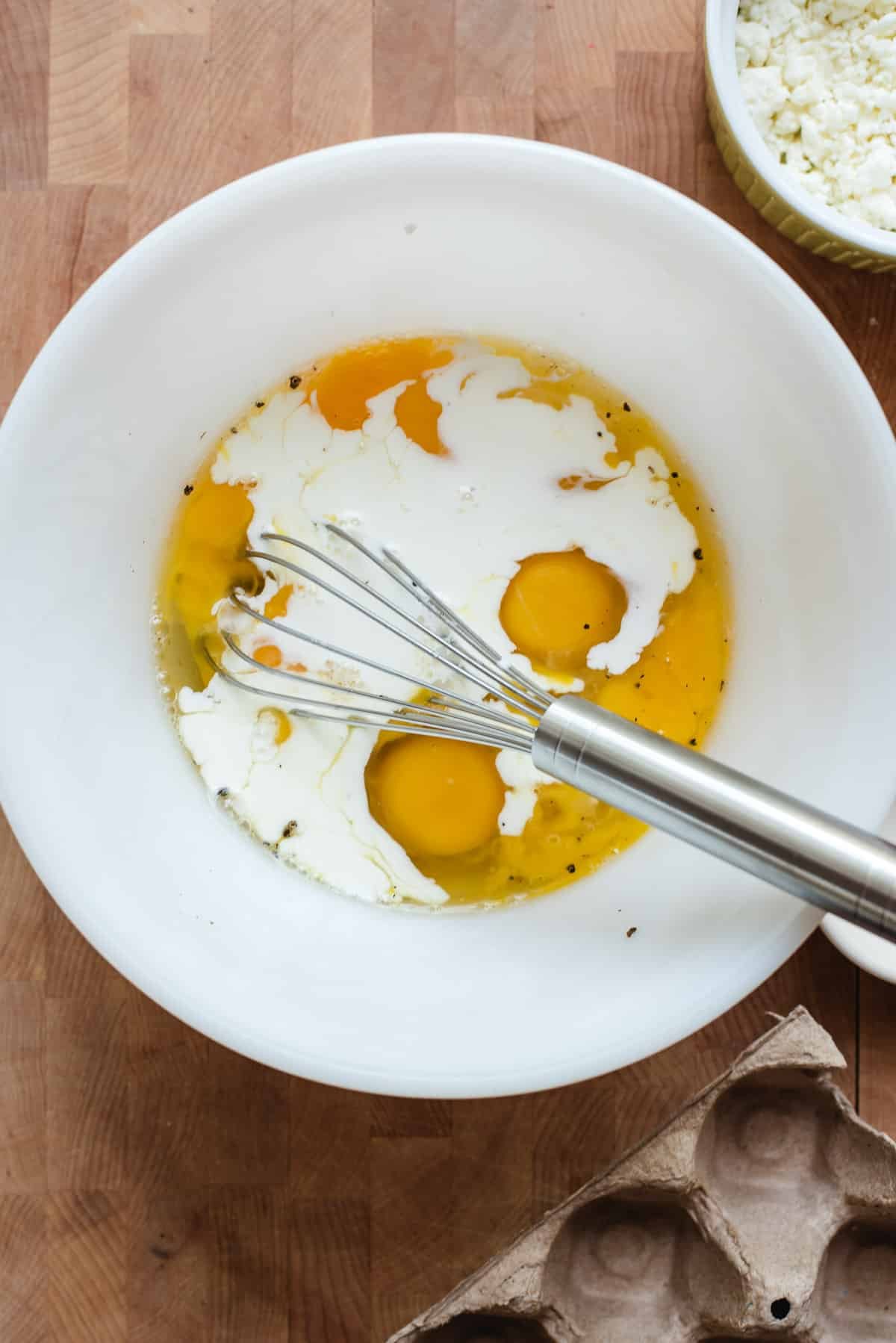 Eggs, half and half, salt and pepper in a white bowl with a whisk.