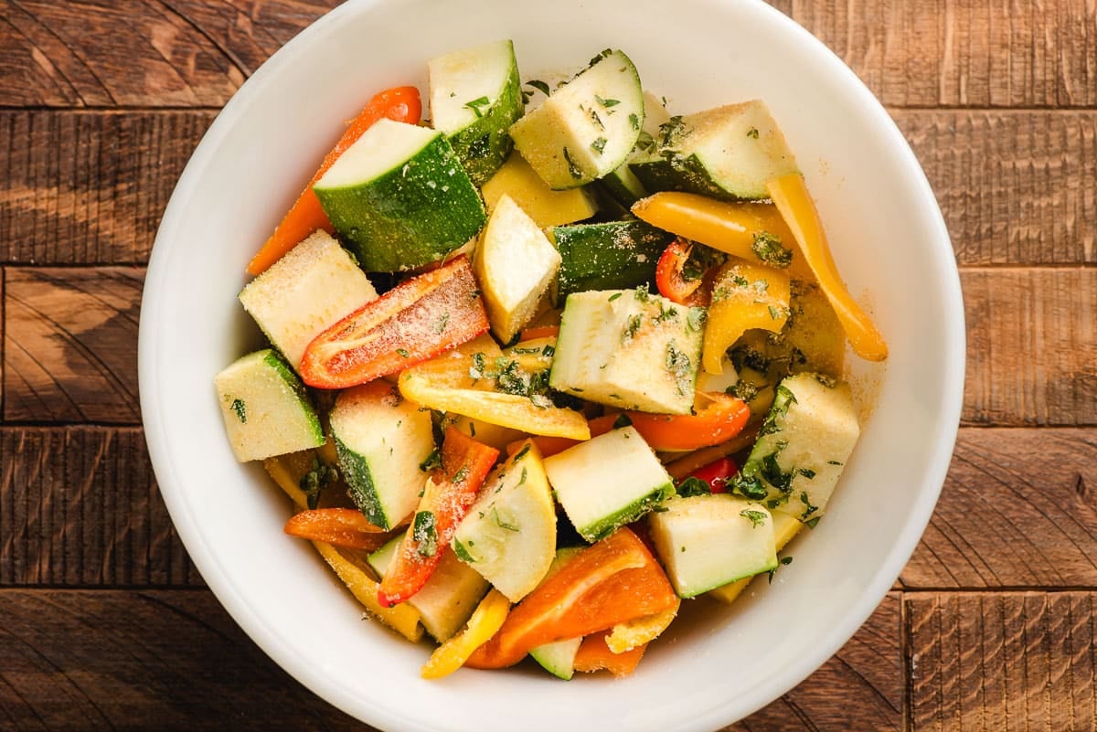 Zucchini and peppers in a bowl with olive oil, herbs, and seasonings.