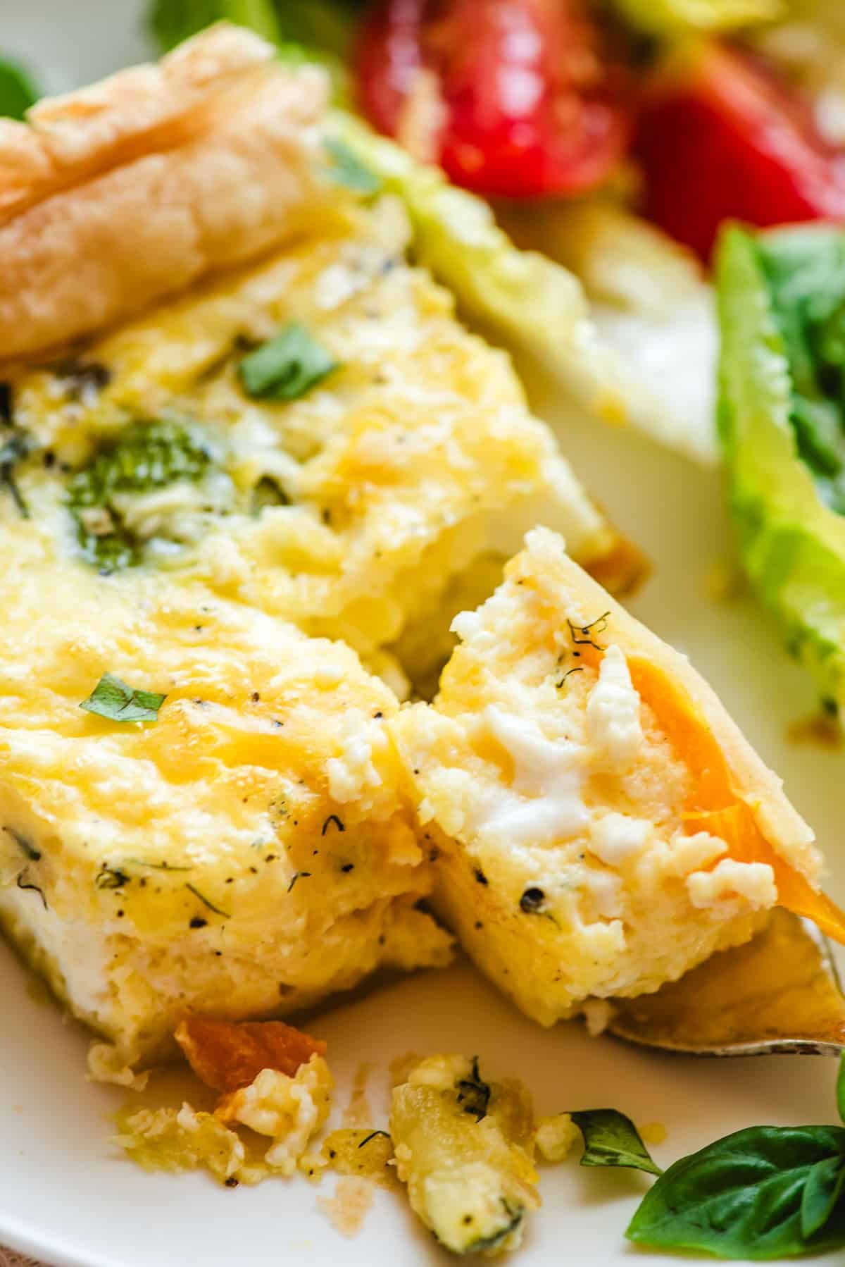 Forkful of roasted vegetable quiche on a white plate.