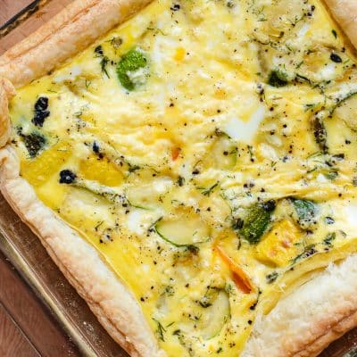 Puff pastry quiche with roasted vegetables and feta cheese in a square baking pan.