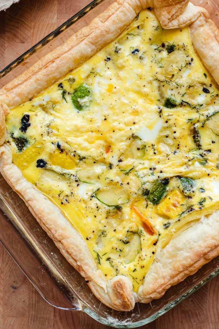 Puff pastry quiche with roasted vegetables and feta cheese in a square baking pan.