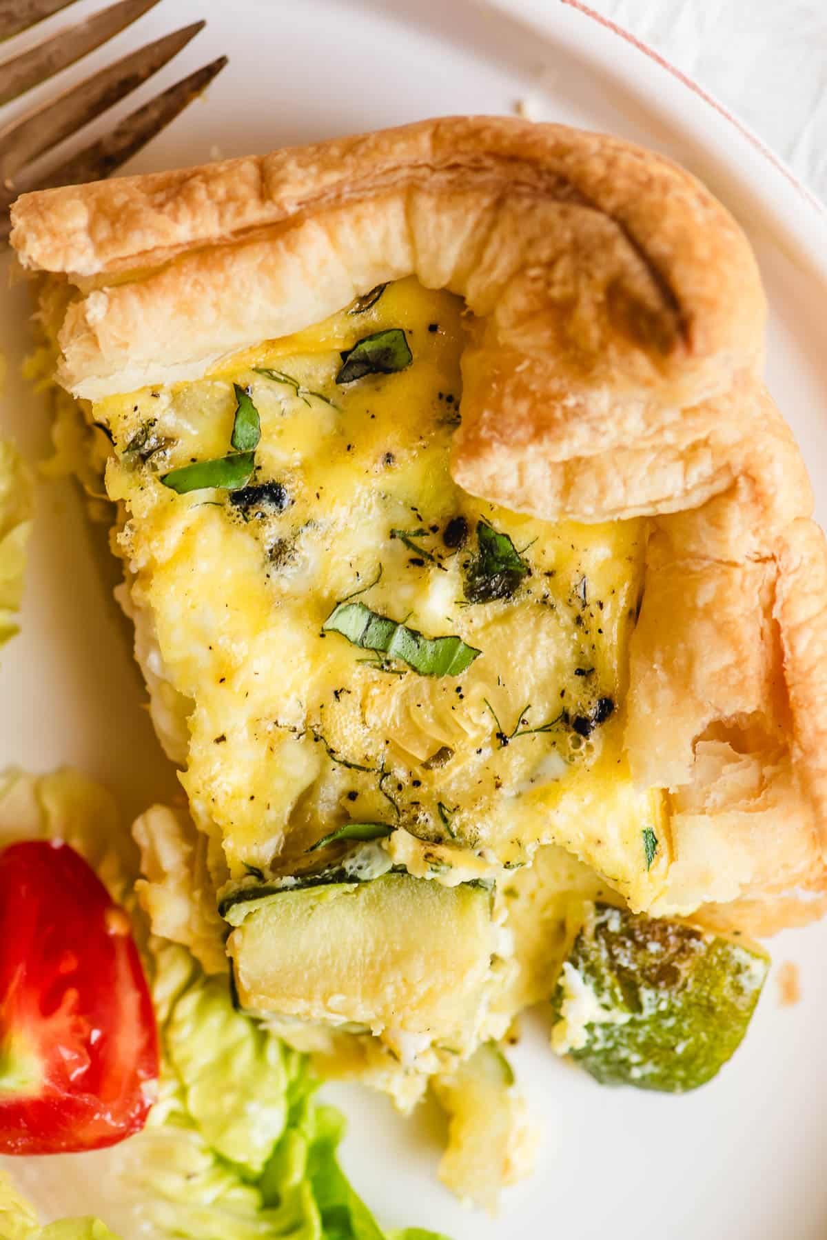 Slice of puff pastry quiche with roasted veggies on a white plate.