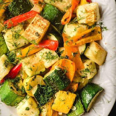 Roasted zucchini and peppers topped with fresh herbs, on a white serving platter.